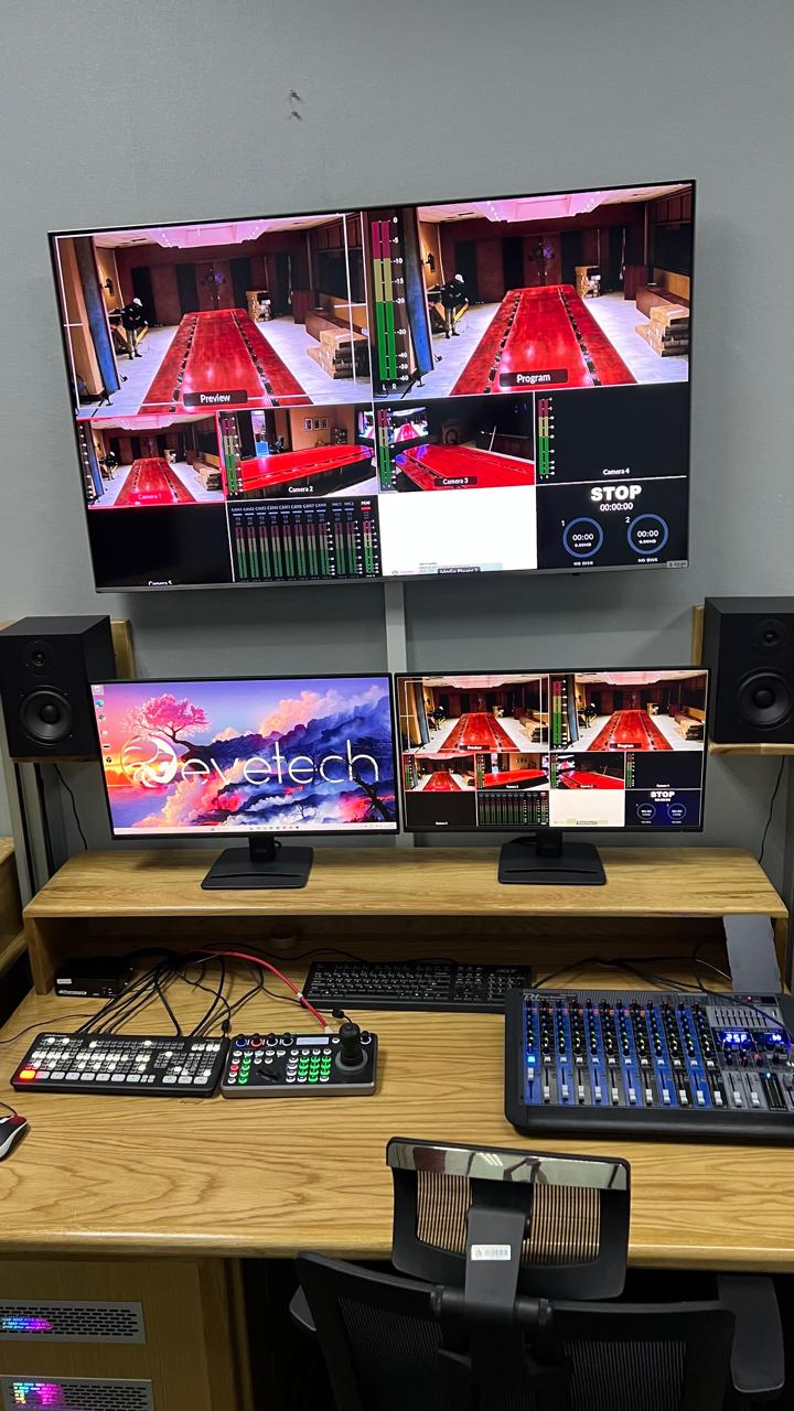 Mojapele edit and production control suite: a multiviewer wall showing preview, program and camera feeds above dual operator displays, with a vision switcher, camera controller and audio mixer on the desk